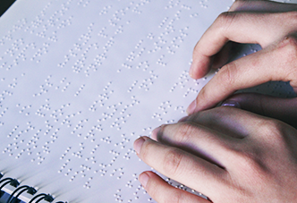 Foto de close de duas mãos em um caderno em braille.